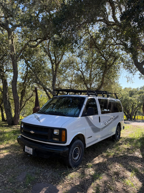 White Chevy camper van, great for an rv rental, parked under mossy oak trees with a giraffe statue in background.