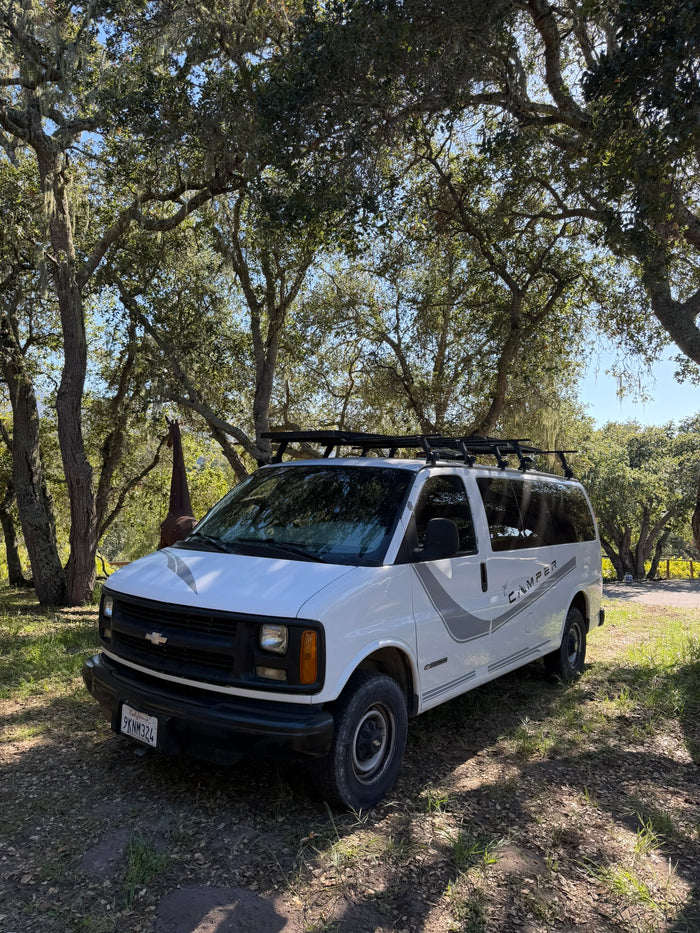 White Chevy camper van, great for an rv rental, parked under mossy oak trees with a giraffe statue in background.