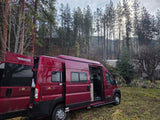 Red Winnebago Solis RV rental parked in a forest clearing with its side and rear doors open.
