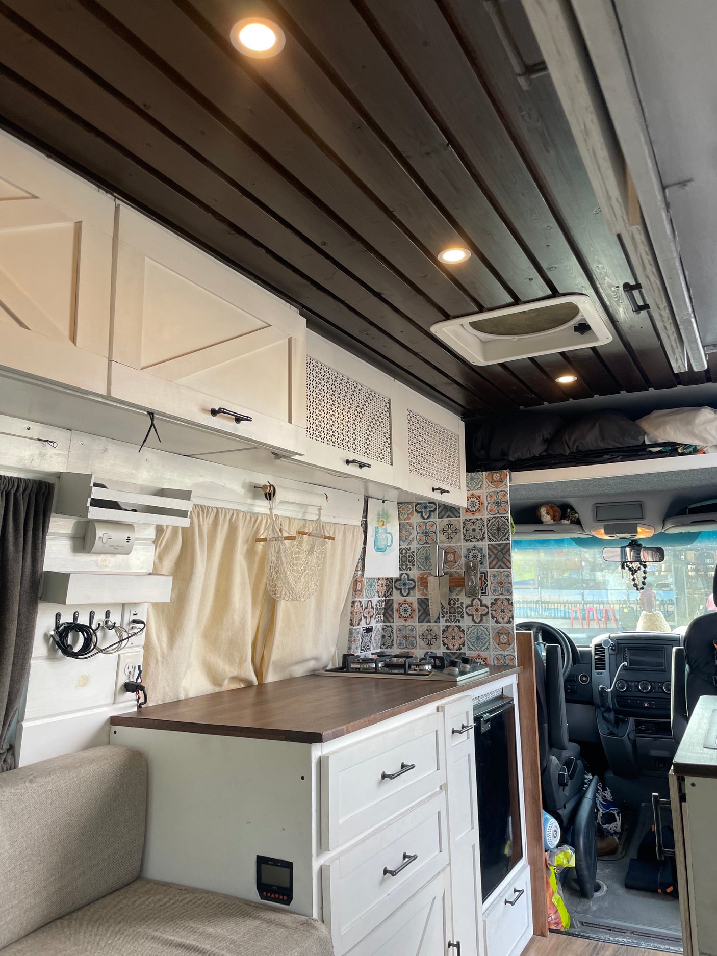 Inside this cozy RV rental: a modern camper van interior with a well-equipped kitchenette, stylish dark wood ceiling, and white cabinetry.