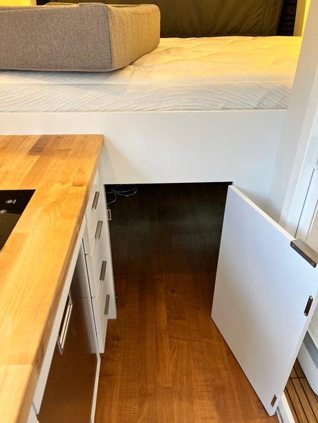 RV rental: Compact interior with a raised bed, modern kitchen counter, and under-bed storage accessible via an open door.