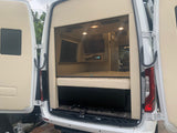 RV rental: View of a modern camper van's custom interior with bed, TV, and lights, seen from the open rear doors.
