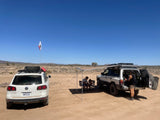Two SUVs are set up for desert camping, with an awning extended and people relaxing in the shade, ideal for an RV rental adventure.
