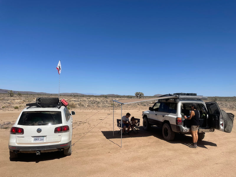 Two SUVs are set up for desert camping, with an awning extended and people relaxing in the shade, ideal for an RV rental adventure. — photo 10