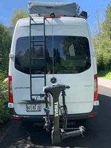White Mercedes Sprinter van with a Thule roof tent & bike rack on the rear, an ideal setup for an rv rental.