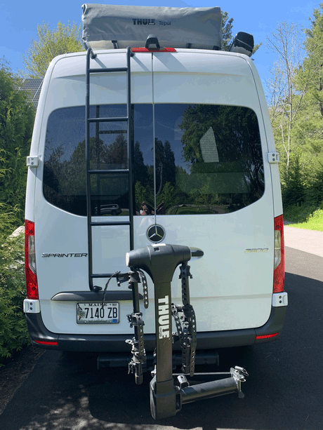 White Mercedes Sprinter van with a Thule roof tent & bike rack on the rear, an ideal setup for an rv rental.