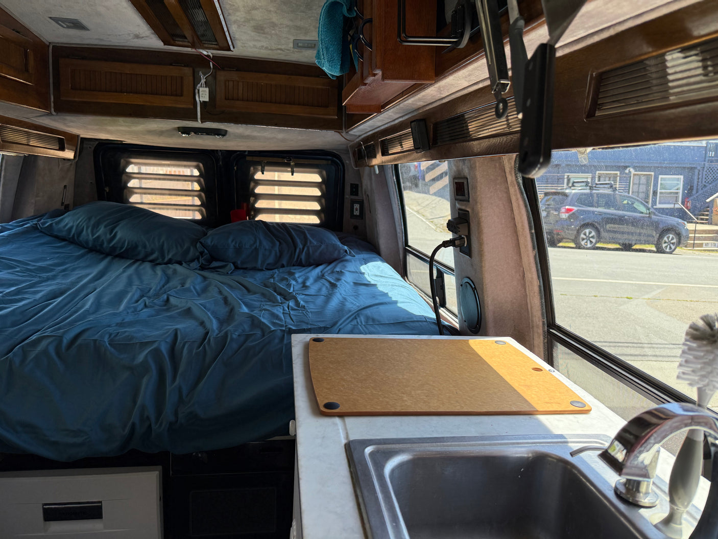 Cozy RV rental interior with blue bed, kitchenette, and sink. Perfect for travel adventures, viewing street outside.