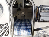 Explore this cozy teardrop RV rental! Inside, a plaid bed is visible through the open arched door, ready for camping adventures.