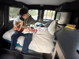 Young man playing guitar on the cozy bed of an RV rental, enjoying music during his journey.