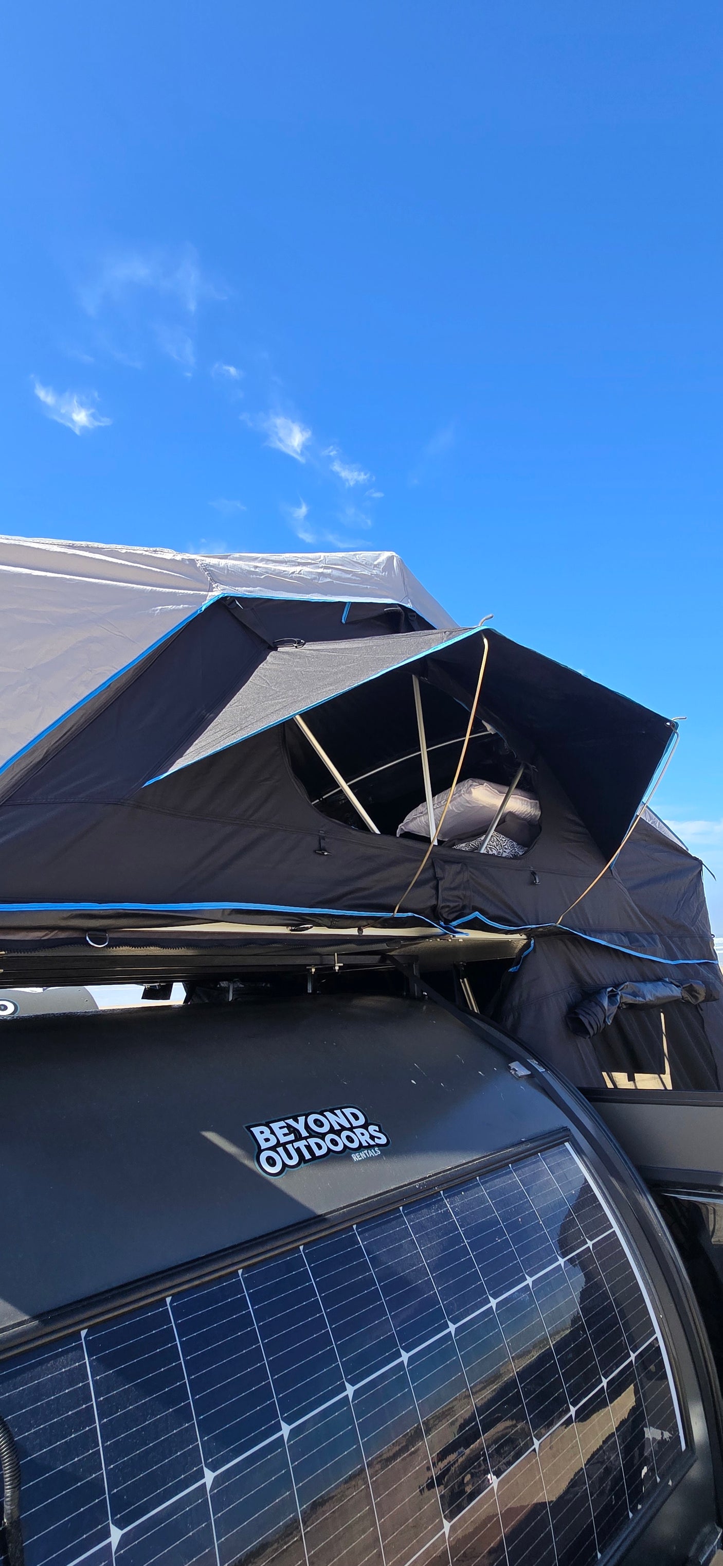 This Beyond Outdoors RV rental features a rooftop tent & solar panel for off-grid camping under a clear blue sky.