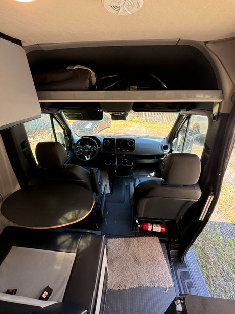 Wide-angle view inside an RV rental, featuring the driver's cockpit, front seats, and a rear dining table.