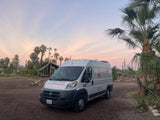 White Magic Outdoor Experiences RV rental van at sunset, surrounded by palm trees on a dirt lot.