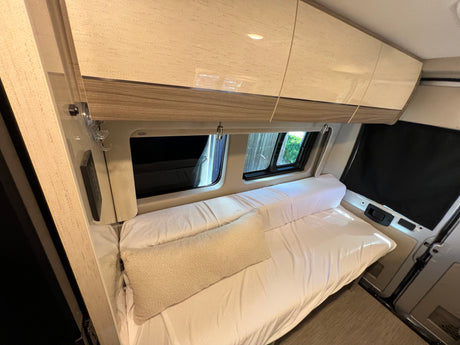 A cozy RV rental interior featuring a neatly made bed, spacious overhead cabinets, and windows, offering comfort and convenience.