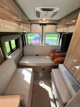 Interior of a modern RV rental, featuring light-colored benches converting to a bed, overhead cabinets, and a view out the back.