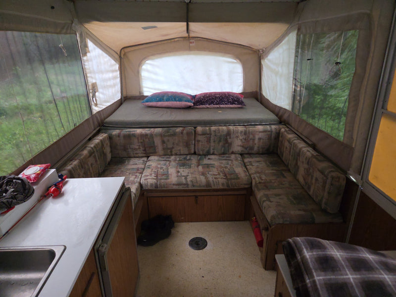  is set up outdoors on grass with its canvas and mesh windows extended.|Interior of an rv rental pop-up camper with a bed — photo 2