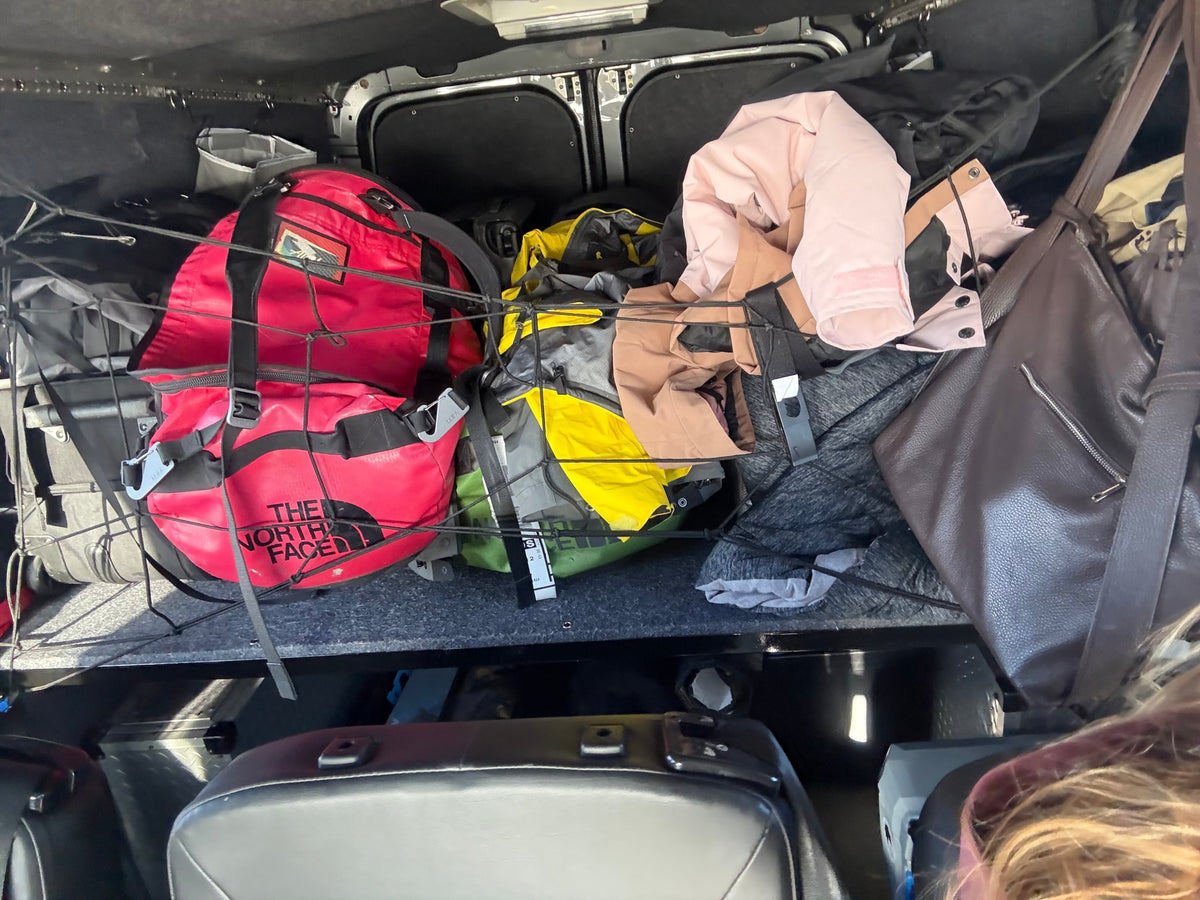 Packed RV rental: Red & yellow North Face bags, clothes, and gear secured by a cargo net in the back for travel. — photo 18