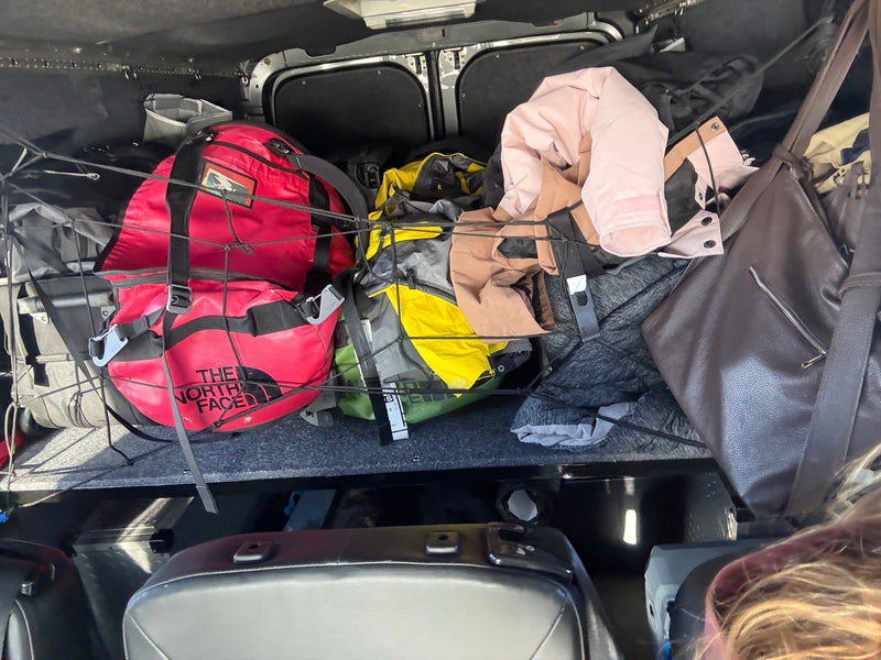 Packed RV rental: Red & yellow North Face bags, clothes, and gear secured by a cargo net in the back for travel. — photo 18