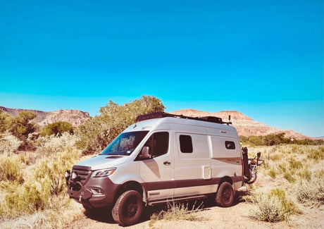 Silver Winnebago Revel camper van in a desert landscape with mountains, ideal for an rv rental adventure.