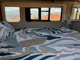 Enjoy breathtaking red rock and snow-capped mountain views from a cozy RV rental bed with patterned bedding and nearby sink.