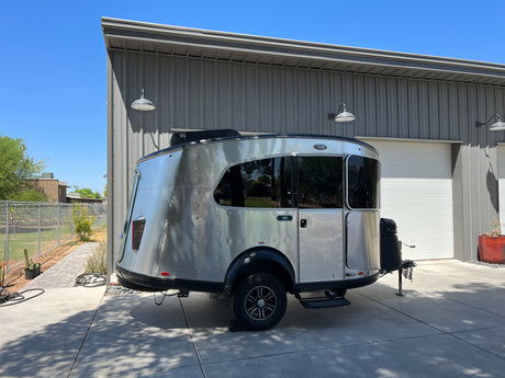 A silver RV rental is parked outside a gray metal building under a clear blue sky, ready for outdoor adventures.