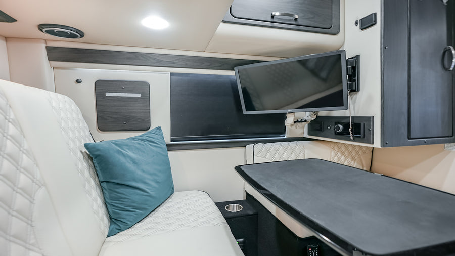 Spacious rv rental interior showing white quilted seating, a large table, and a mounted TV, ideal for comfortable travel or work.