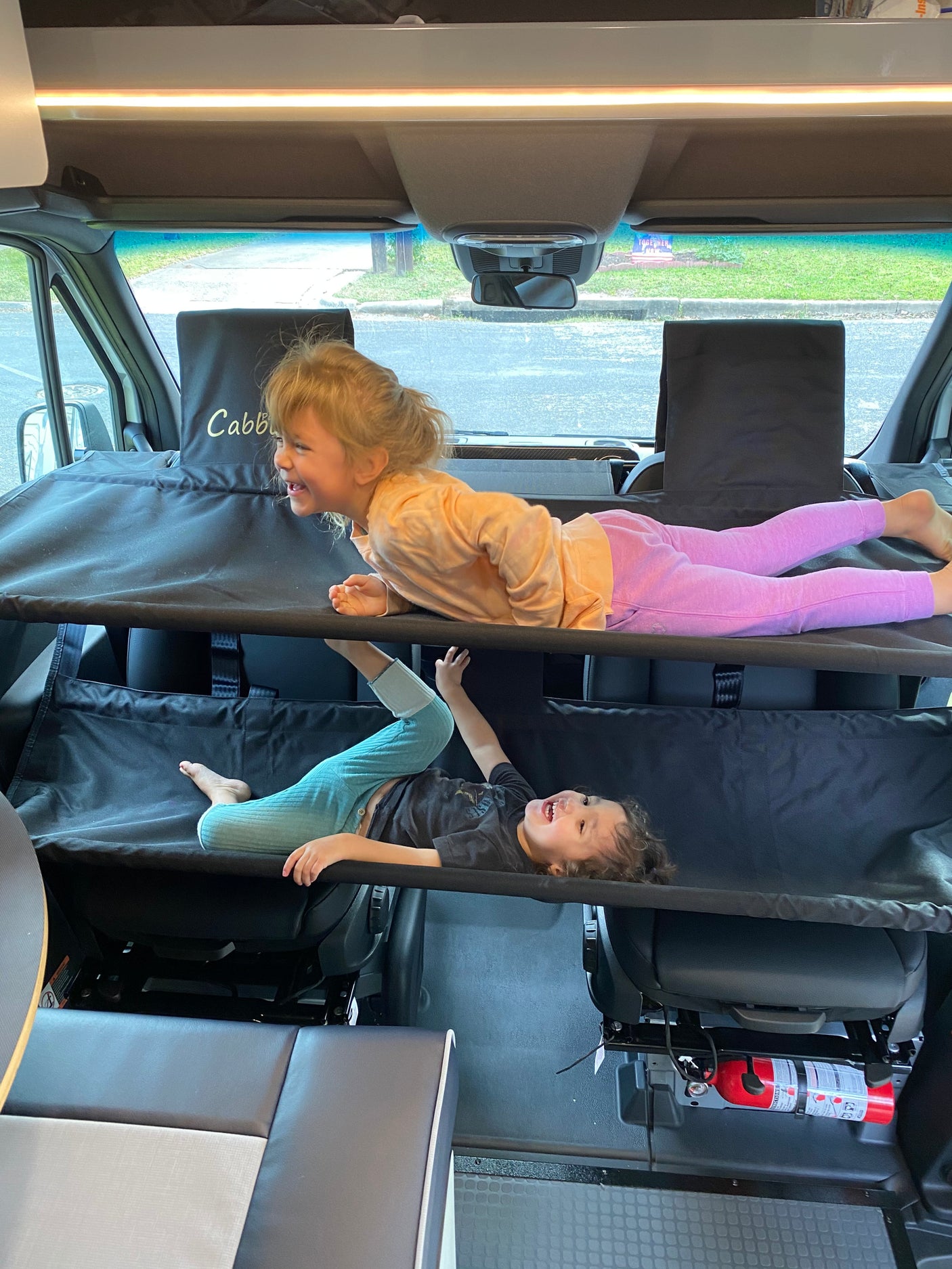 Two happy kids play on a two-tier bunk system in an RV rental camper van. Laughter fills the family road trip space.