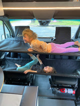 Two happy kids play on a two-tier bunk system in an RV rental camper van. Laughter fills the family road trip space.