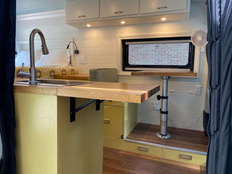  grassy field with distant trees under a clear blue sky.|RV rental's open side door showcases a custom interior: compact kitchen