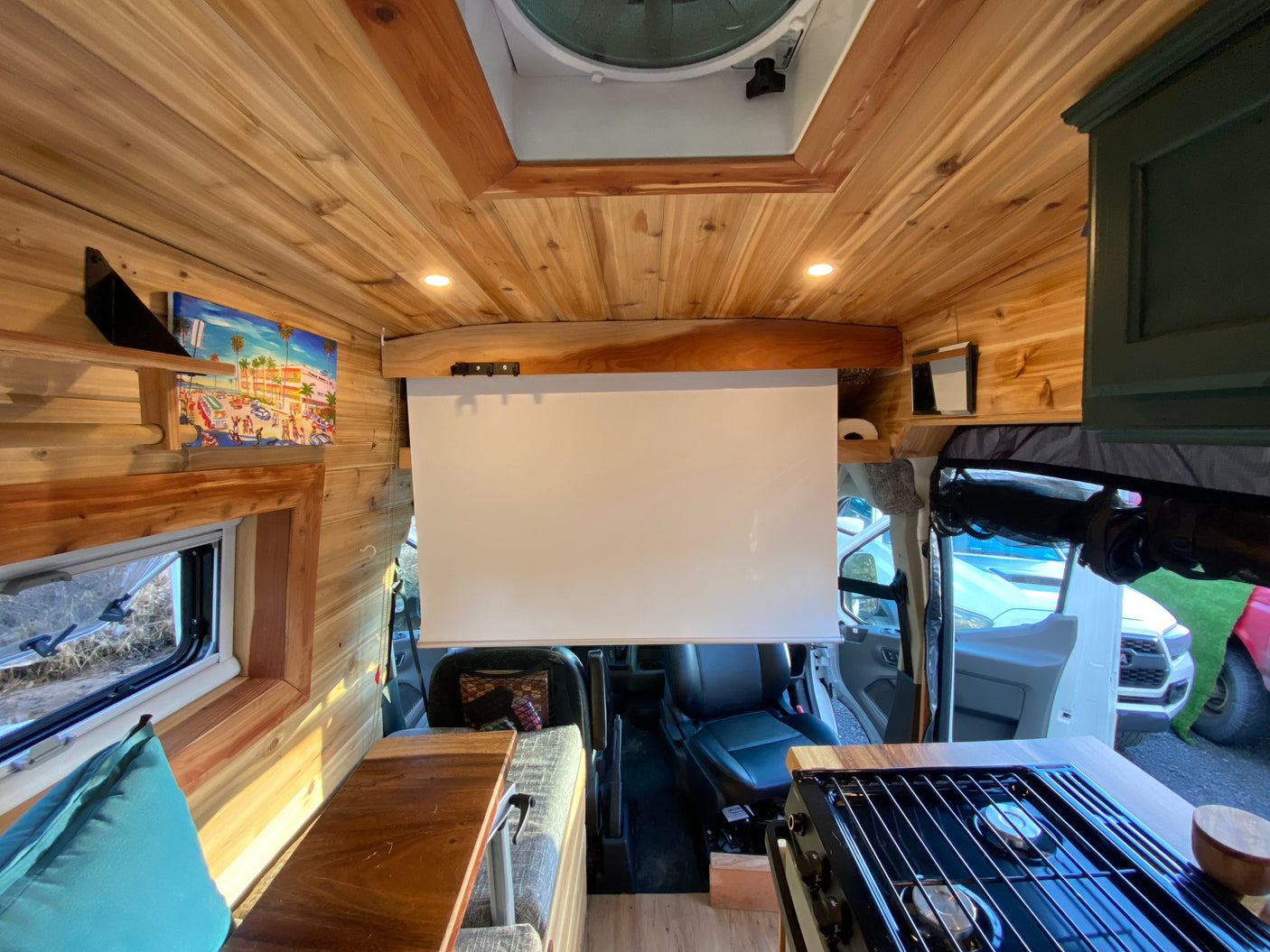 Cozy camper van interior for RV rental, featuring wood accents, a projector screen, and compact kitchen.