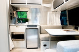 Bright RV rental interior featuring a compact kitchen with sink, fridge, microwave, and a cozy dining area.