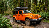 An orange Jeep Wrangler with a roof-top tent navigates a muddy forest trail. Explore nature with an RV rental!