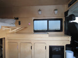 Explore this rv rental's compact wood interior, featuring a cozy bed, kitchen counter, and fridge, ideal for adventures.