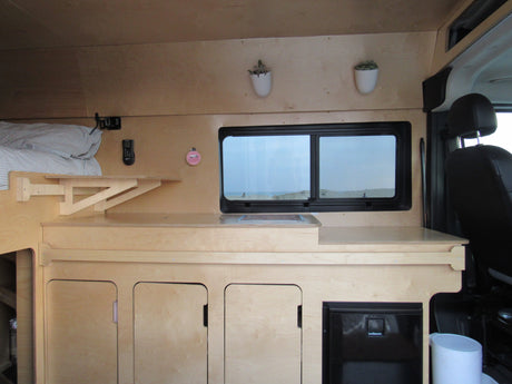 Explore this rv rental's compact wood interior, featuring a cozy bed, kitchen counter, and fridge, ideal for adventures.