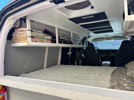 RV rental's cozy camper van interior features a bed, custom overhead storage with towels, and a ceiling fan.