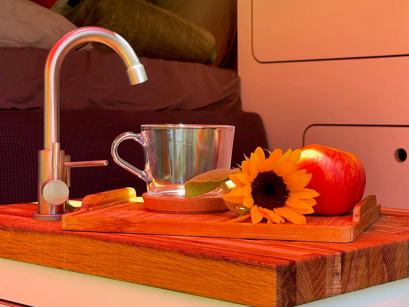 Enjoy comfort in your RV rental! Modern faucet, clear mug, apple & sunflower on a wooden tray, showing a cozy camper interior.