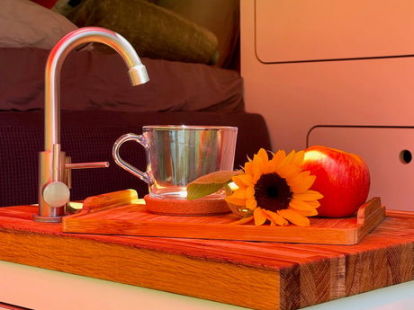 Enjoy comfort in your RV rental! Modern faucet, clear mug, apple & sunflower on a wooden tray, showing a cozy camper interior.