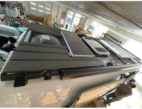 Rooftop setup for an RV rental: solar panels, AC unit, and a custom deck with lights on a white camper van. Ready for adventure.
