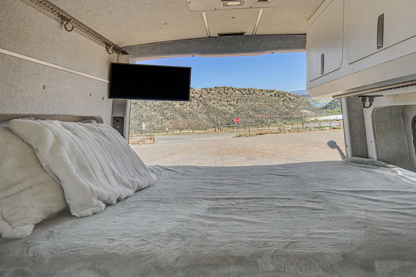 Cozy rv rental bed with plush pillows looking out to a scenic mountain landscape and road.