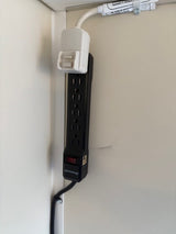 Wall-mounted Dewenweld power strip with a white adapter in an RV rental, neatly secured for tidy power access.