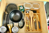 An organized RV rental kitchen drawer featuring plates, bowls, gold cutlery, and reusable travel essentials.