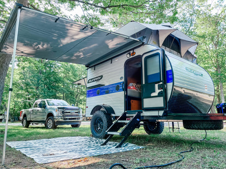 Sunray Sport RV rental: a light-colored camper with awning & rooftop tent, setup for camping next to a Ford truck on a green site.