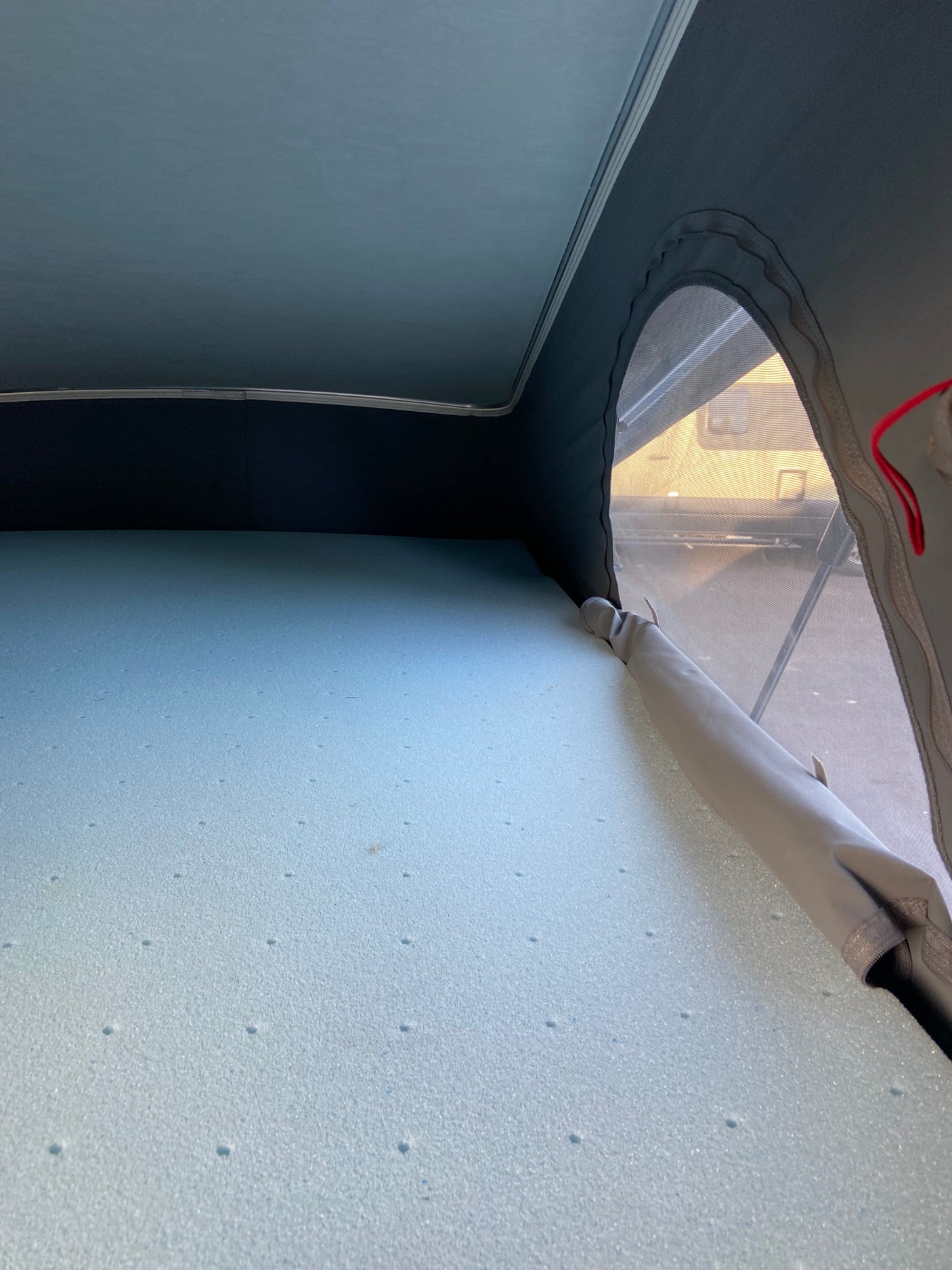 Comfortable foam mattress inside an RV rental's pop-top sleeping area, with a mesh window offering a sunny view.