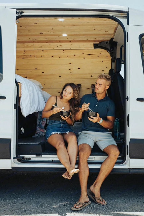 A couple enjoys a quiet meal inside their white RV rental, sitting by the open back door.