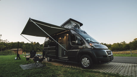 This RV rental camper van is set up for a relaxing campsite adventure, with an awning extended & pop-top raised.