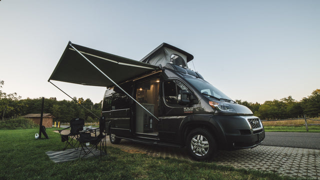 This RV rental camper van is set up for a relaxing campsite adventure, with an awning extended & pop-top raised.