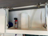 Inside an RV rental overhead cabinet: paper towels, bear spray, and gas struts holding the door open.