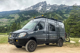 A custom gray Mercedes Sprinter adventure van, an ideal RV rental, parked off-road with stunning mountains & forests.