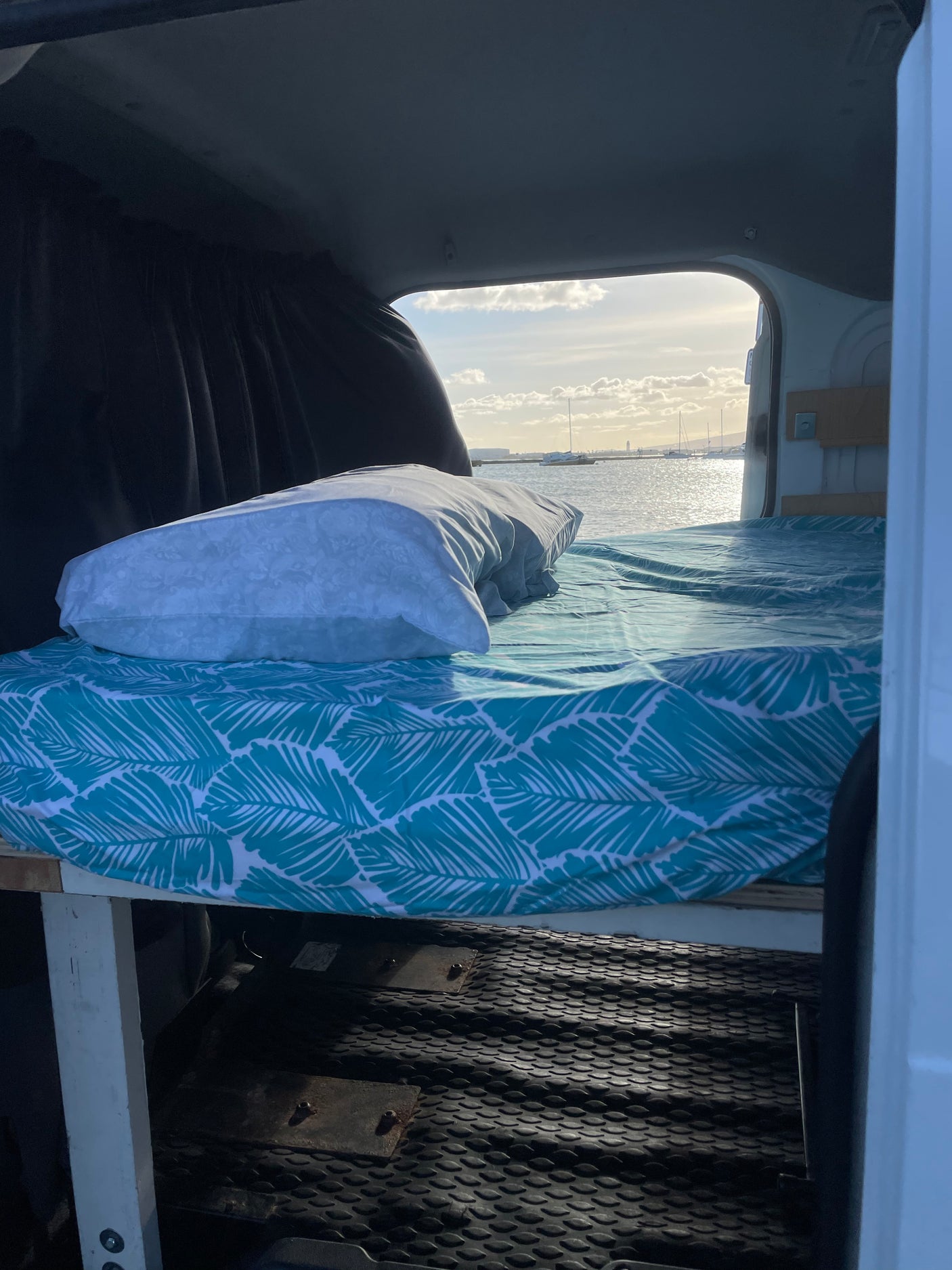 Comfy bed inside an RV rental with an amazing ocean view, sailboats visible. Perfect for scenic travel adventures.