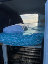Comfy bed inside an RV rental with an amazing ocean view, sailboats visible. Perfect for scenic travel adventures.