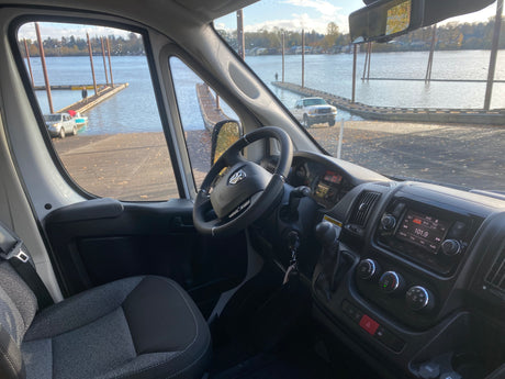 Interior of an RV rental van, looking out at a boat ramp with vehicles and docks extending into the water.